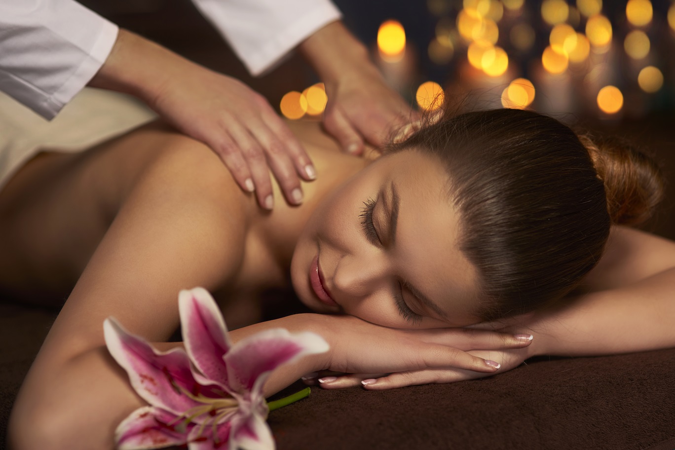 Femme massée sur un lit avec une fleur et des bougies en arrière plan